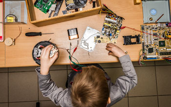 Boy sitting at a desk working on multiple electronic motherboards