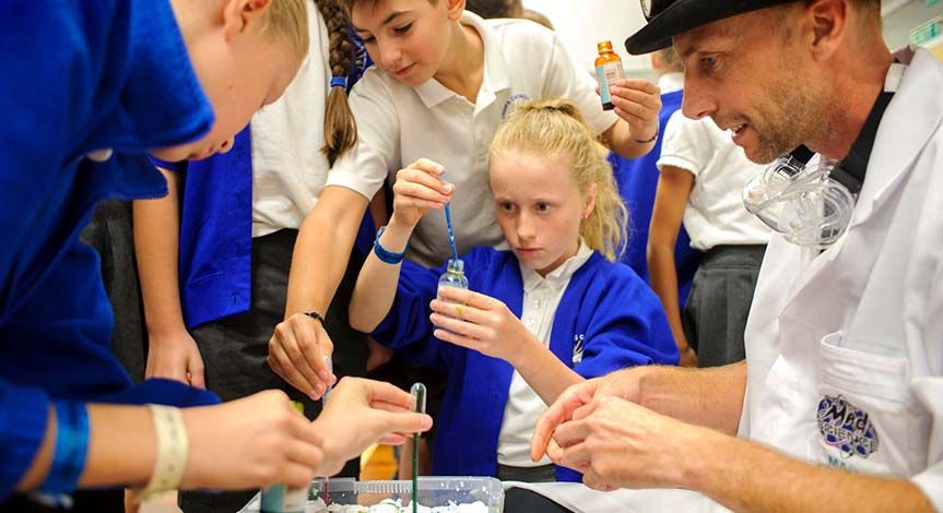 Kids pouring colored liquid from a pipette onto a tray of ice