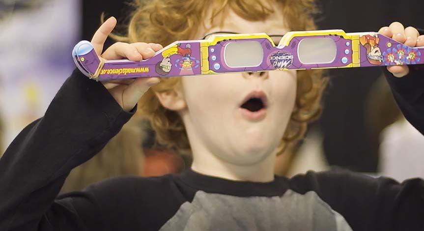 Boy looking surprised holding a stack of Mad Science diffraction glasses