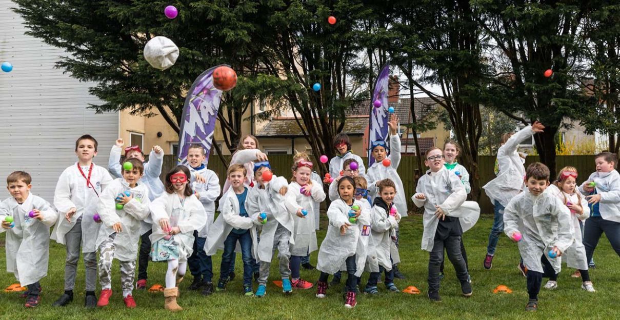 Kids in mad science lab coats throwing colored balls 