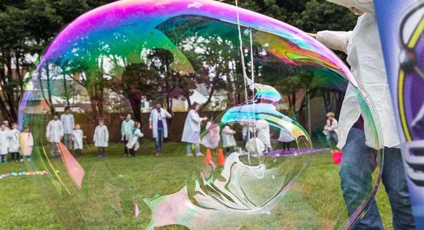A kid in a mad science lab coat making a large bubble on grass