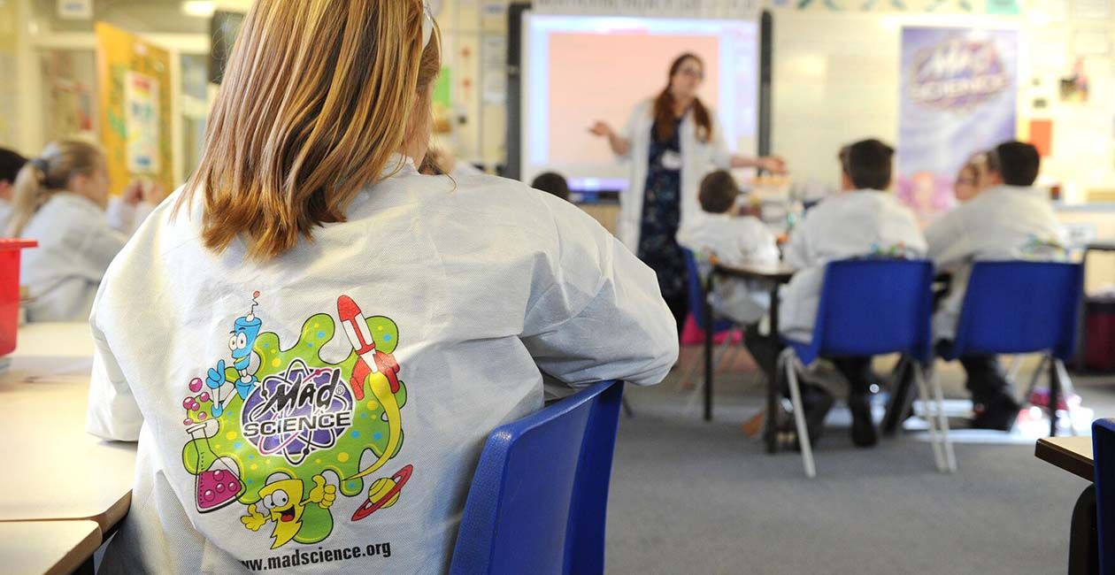 Students sitting at their desks in mad science lab coats listening to their mad scientist teacher