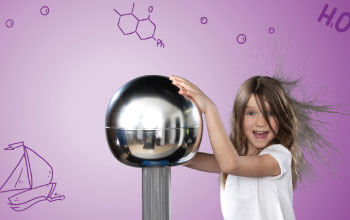 Girl in white shirt coat touching electric silver ball causing her hair to go up.
