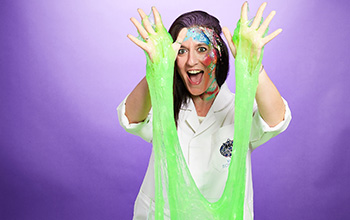Mad scientist with glitter face paint holding hands in the air with slime dripping down.