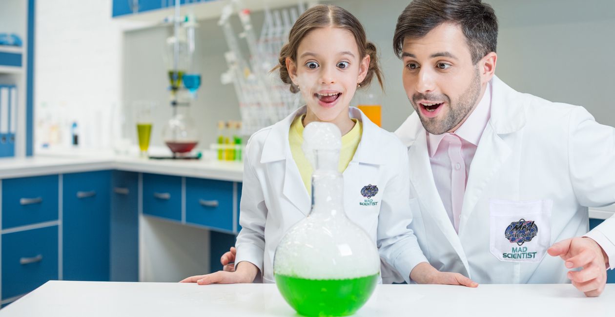 Scientist and little girl in lab looking at a flask with a green liquid inside.