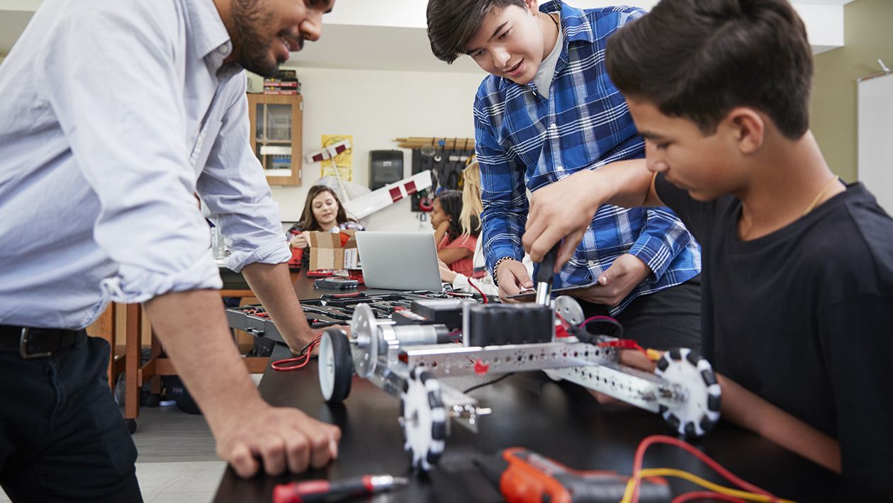 Teacher with male students building robotic vehicle 