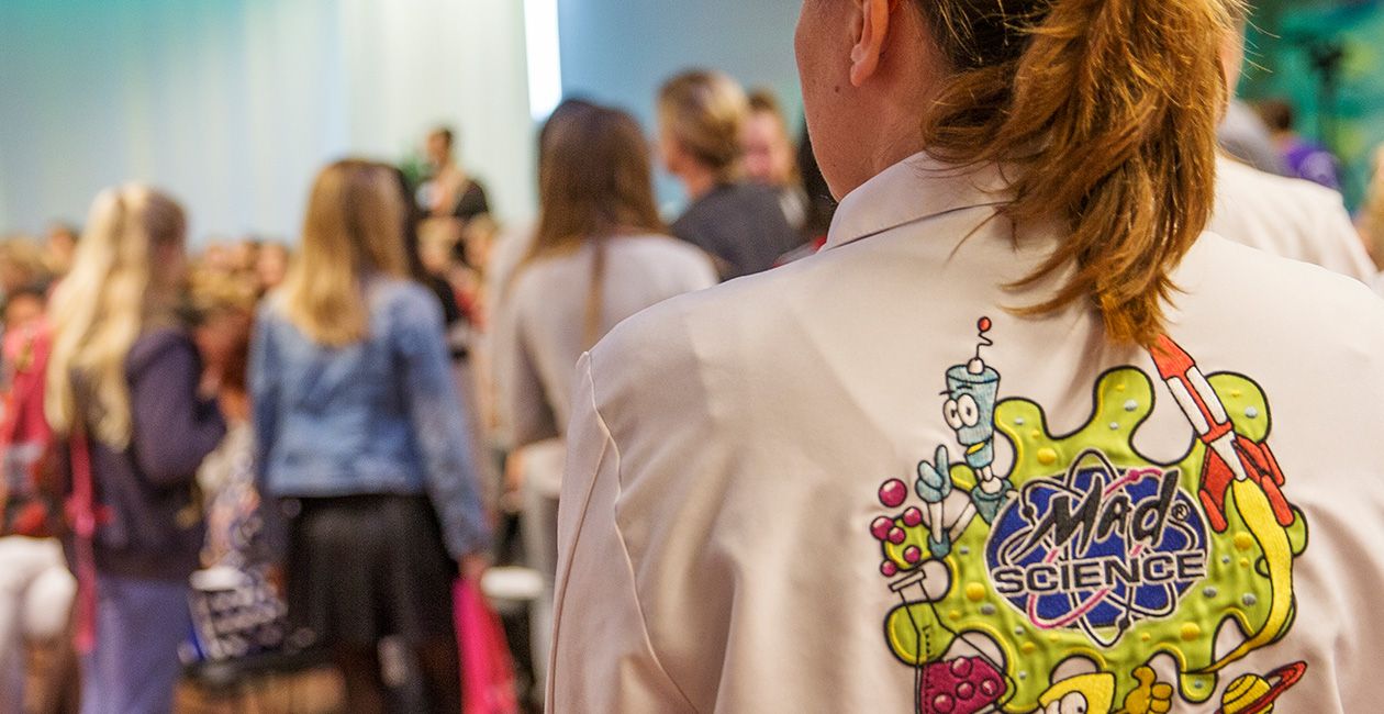 Mad scientist standing wearing a lab coat with the mad science logo on the back of the coat