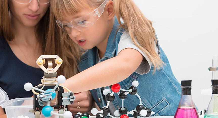 A woman teacher and girl collect molecules and conduct experiments. On the table are a robot and beakers with liquid inside.