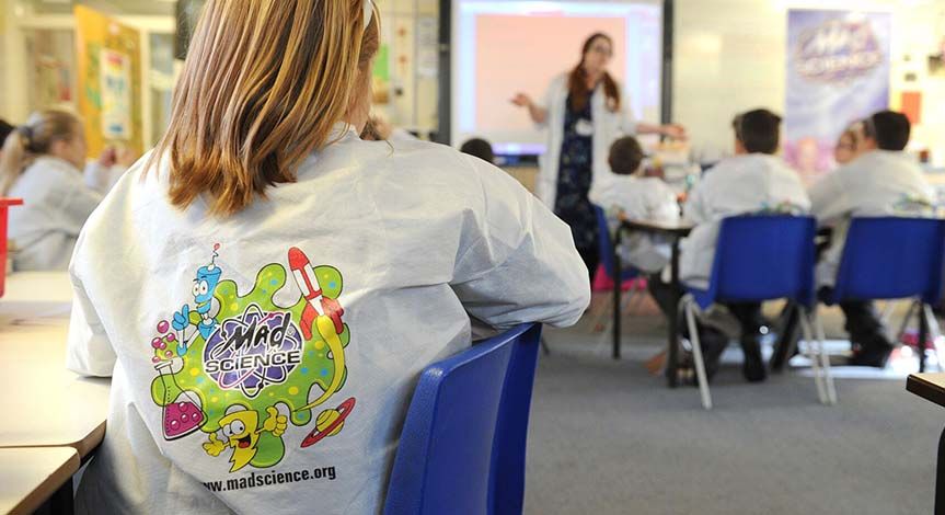 Students sitting at their desks in mad science lab coats listening to their mad scientist teacher